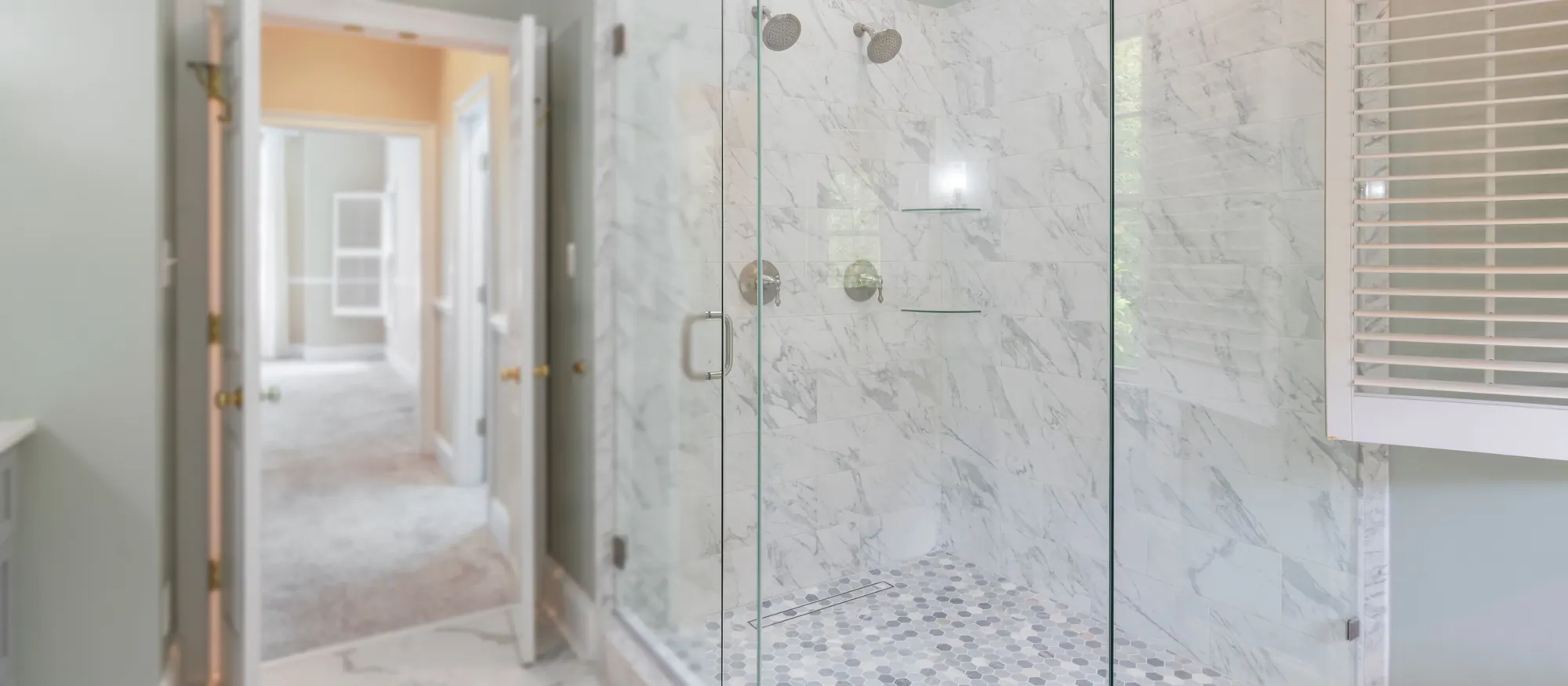 Finished marble walk-in shower with frameless glass doors in a remodeled bathroom