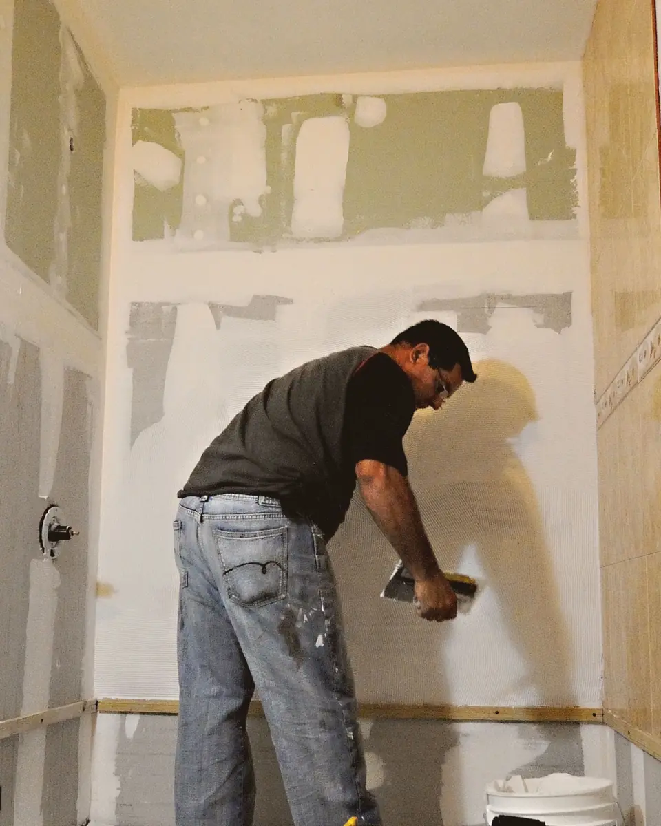Remodeler troweling thinset onto a new shower wall in a bathroom stripped to the studs
