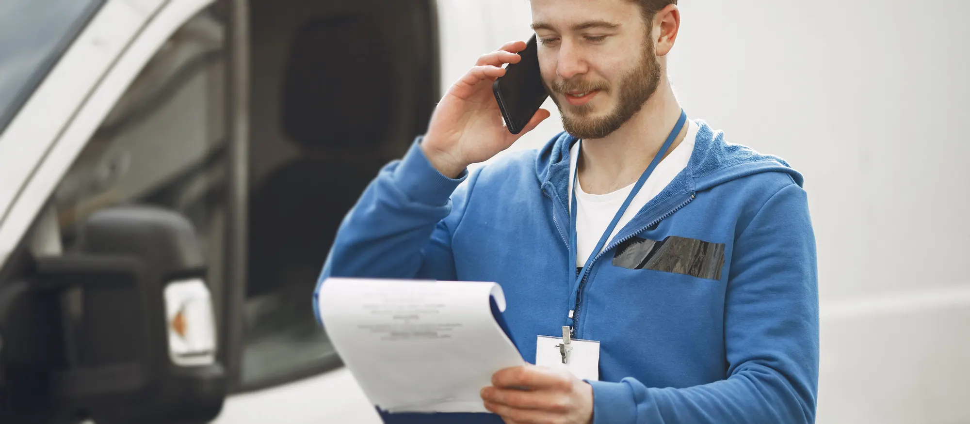 Route owner on a phone call checking a clipboard beside an unmarked white cargo van