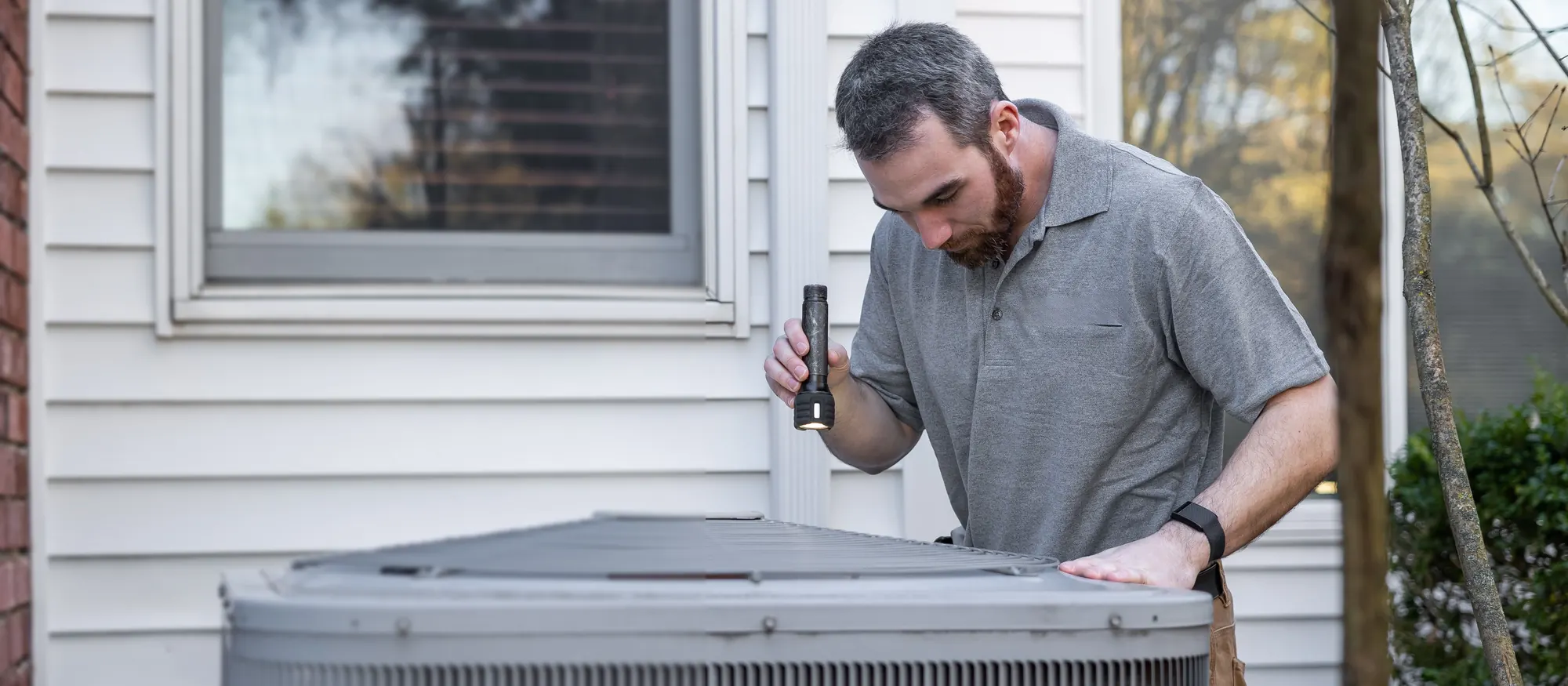 Technician with his hand on top of an outdoor air conditioner condenser beside a house