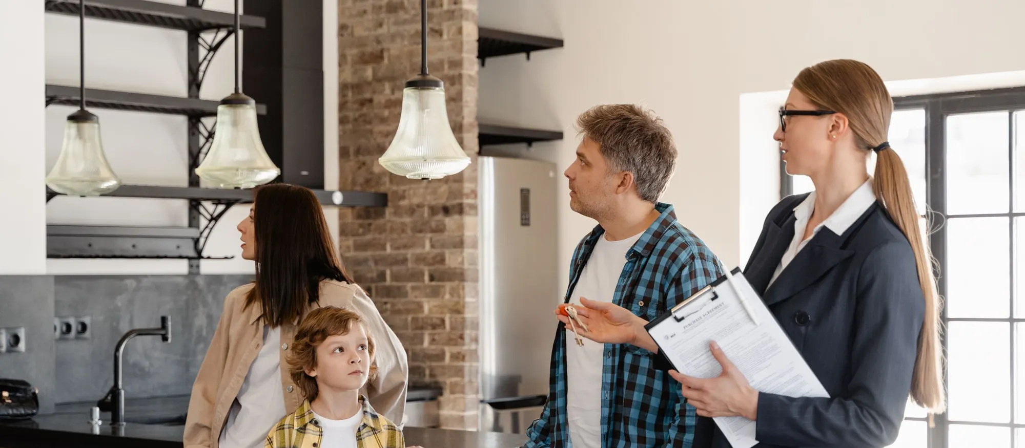 Real estate agent holding a clipboard while walking a family through a home's open kitchen