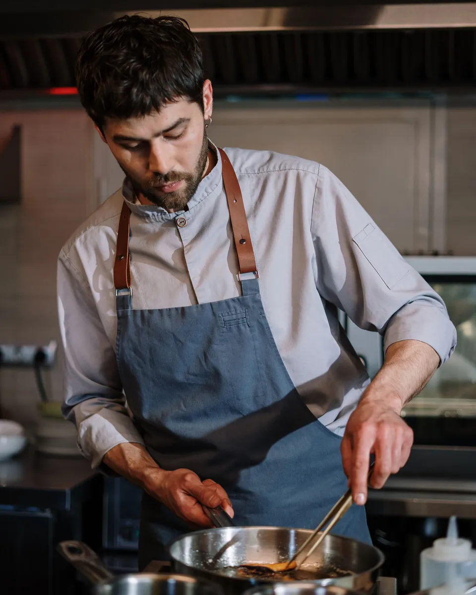 Restaurant cook in a blue apron stirring a pan on the line in a professional kitchen