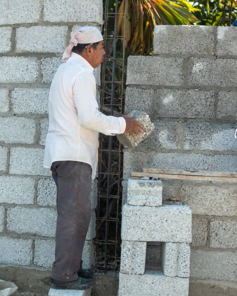 Mason setting a concrete block into a rising CMU wall with rebar in the open cells
