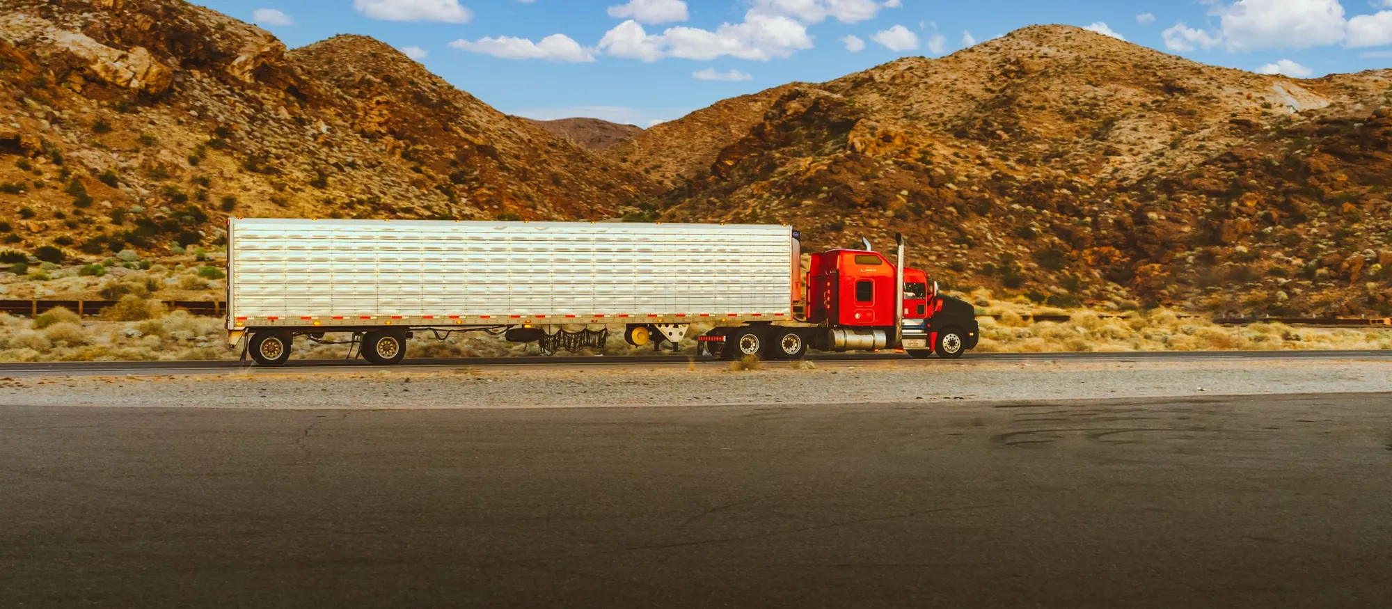 Red semi truck pulling a refrigerated trailer past desert hills