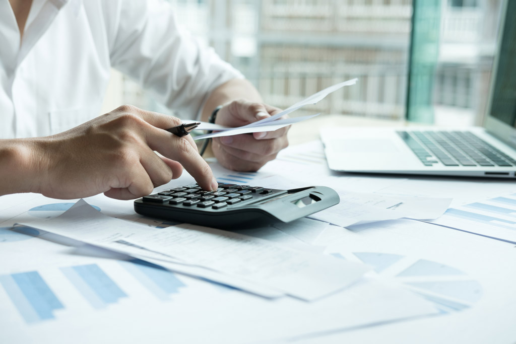 Close up of business professional using calculator surrounded by tax payroll paperwork