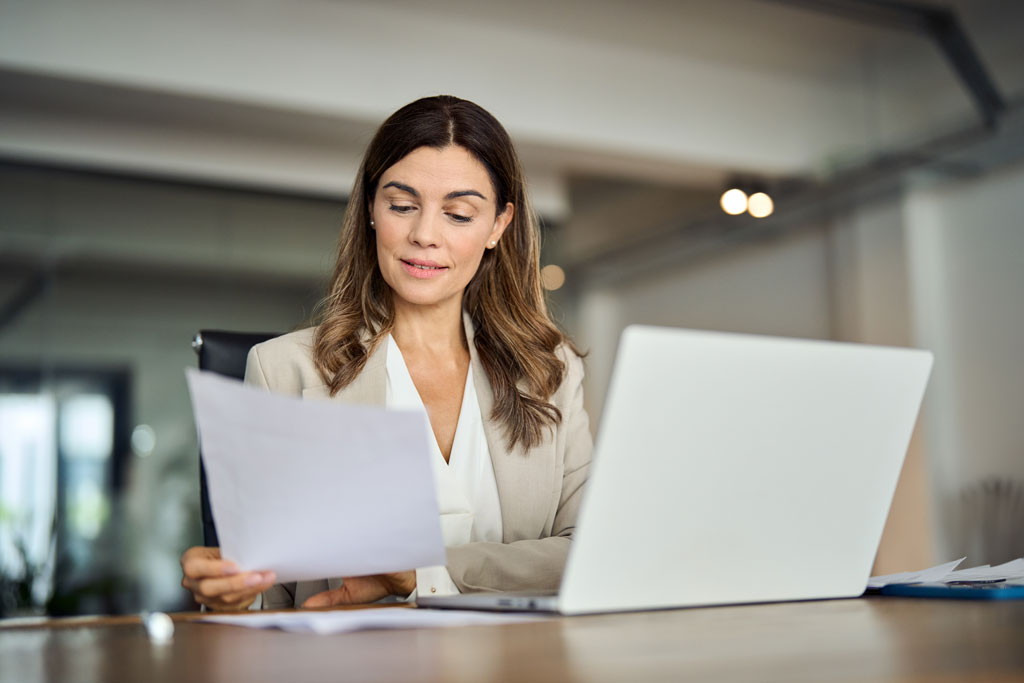 Smart businesswoman handling paperwork and working at desk with laptop